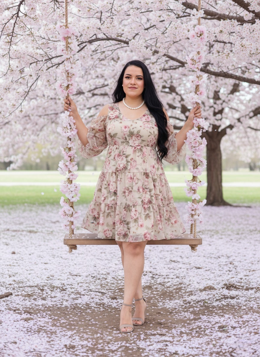 Woman in a floral dress sitting on a swing under cherry blossom trees with snow on the ground.