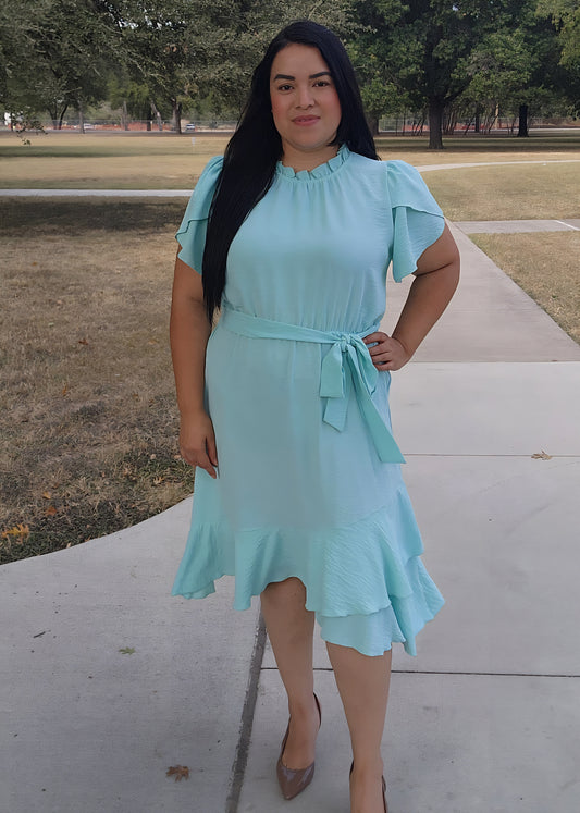 Woman wearing a light blue dress standing on a sidewalk with trees in the background