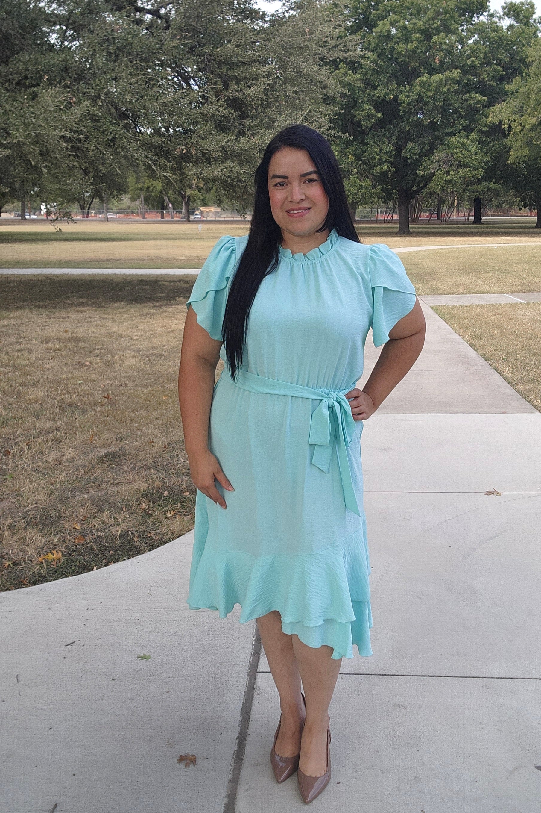 Woman in a light blue dress standing on a sidewalk with trees in the background