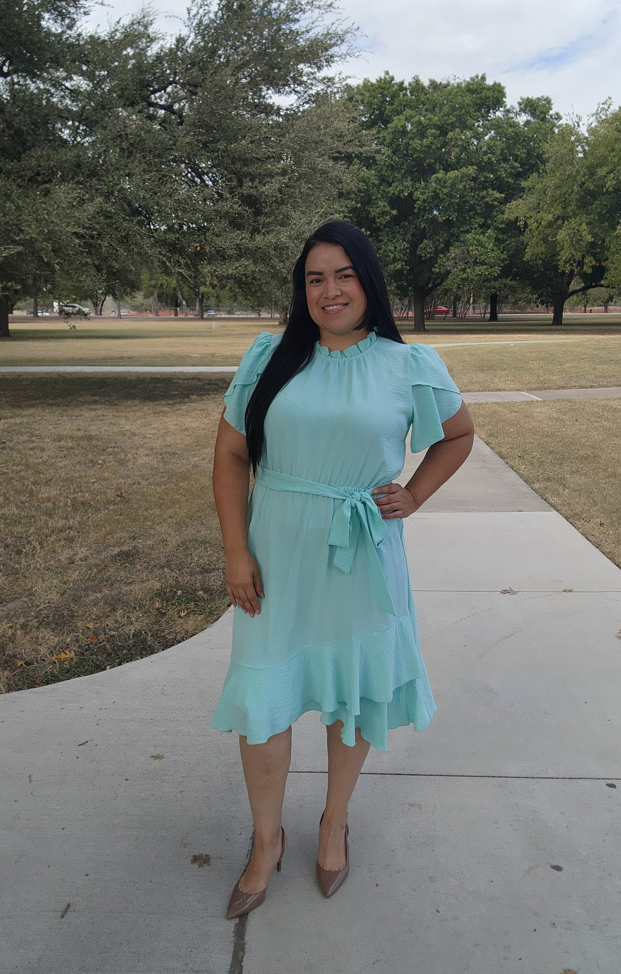 Woman in a light blue dress standing on a sidewalk with trees in the background