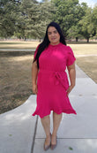 Woman in a pink dress standing on a sidewalk with trees in the background