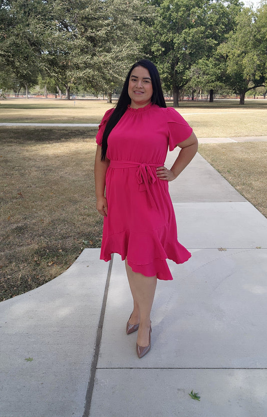 Woman in a pink dress standing on a sidewalk with trees in the background