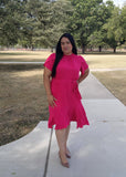 Woman in a pink dress standing on a sidewalk with trees in the background