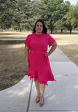 Woman in a pink dress standing on a sidewalk with trees in the background
