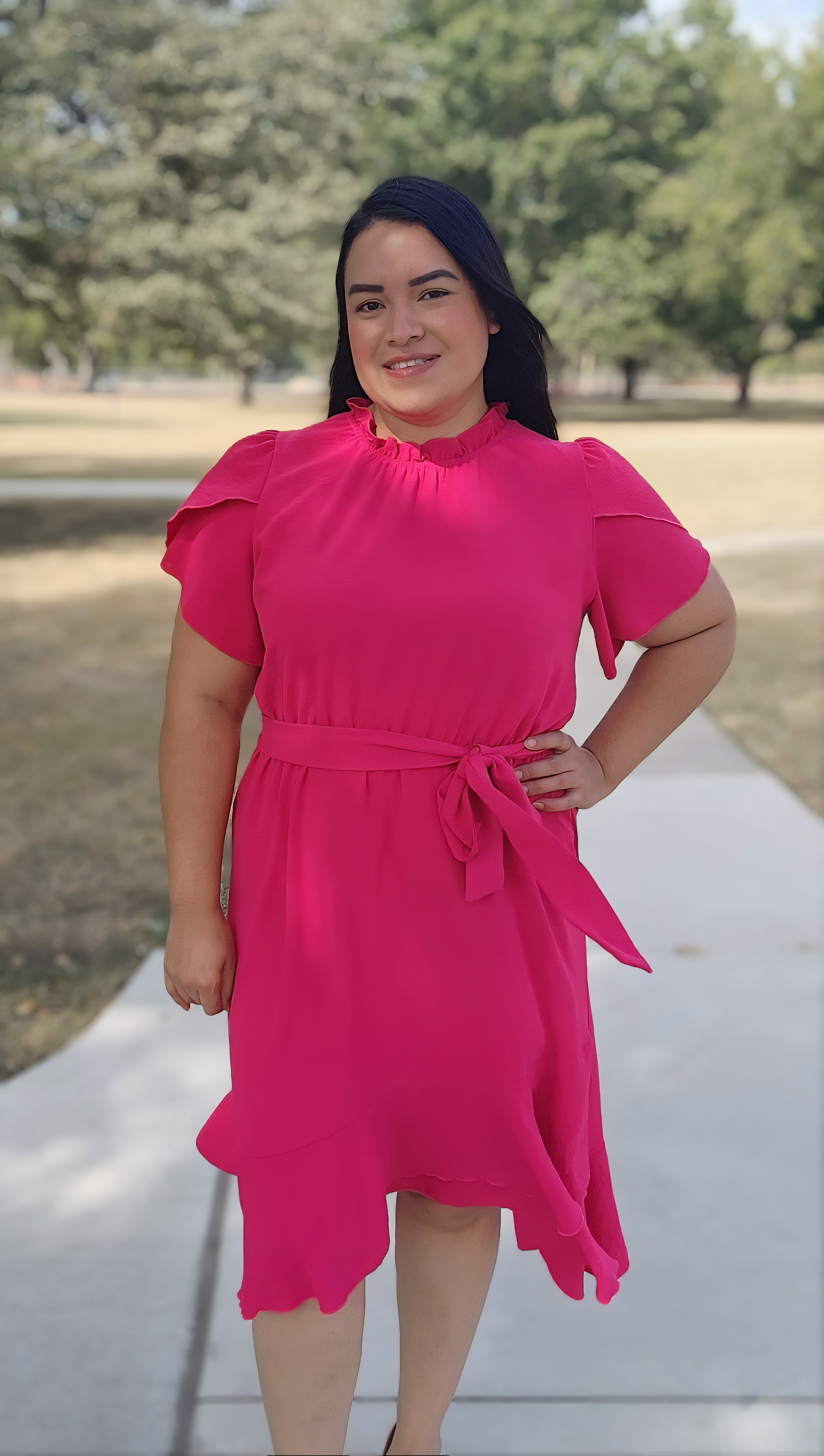 Woman in a bright pink dress standing outdoors on a path with trees in the background