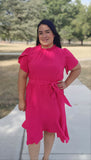 Woman in a bright pink dress standing outdoors on a path with trees in the background