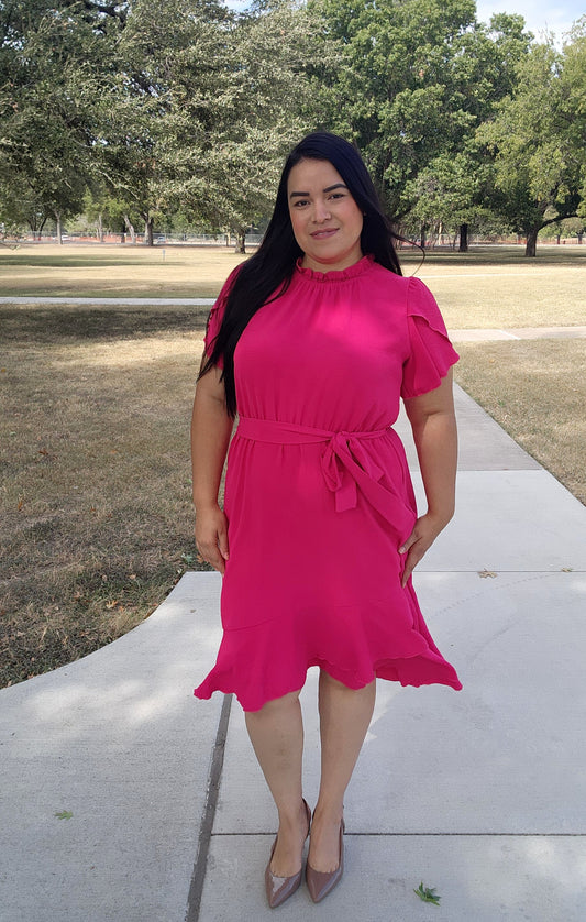 Woman in a pink dress standing on a sidewalk with trees in the background