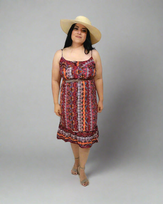 Woman wearing a patterned dress and wide-brimmed hat indoors with a white curtain background.