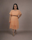 Woman wearing an orange dress with a belt, standing in front of a white curtain.