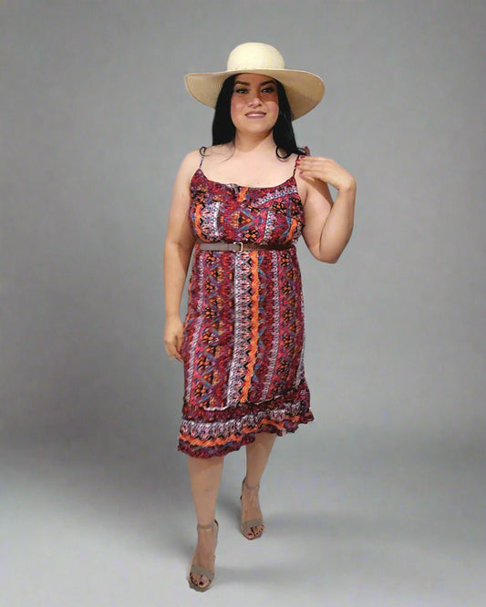 Woman wearing a colorful dress and wide-brimmed hat indoors with a white curtain background.