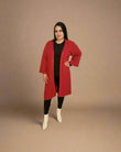 Woman wearing a red coat, black top, and white boots on a beige background